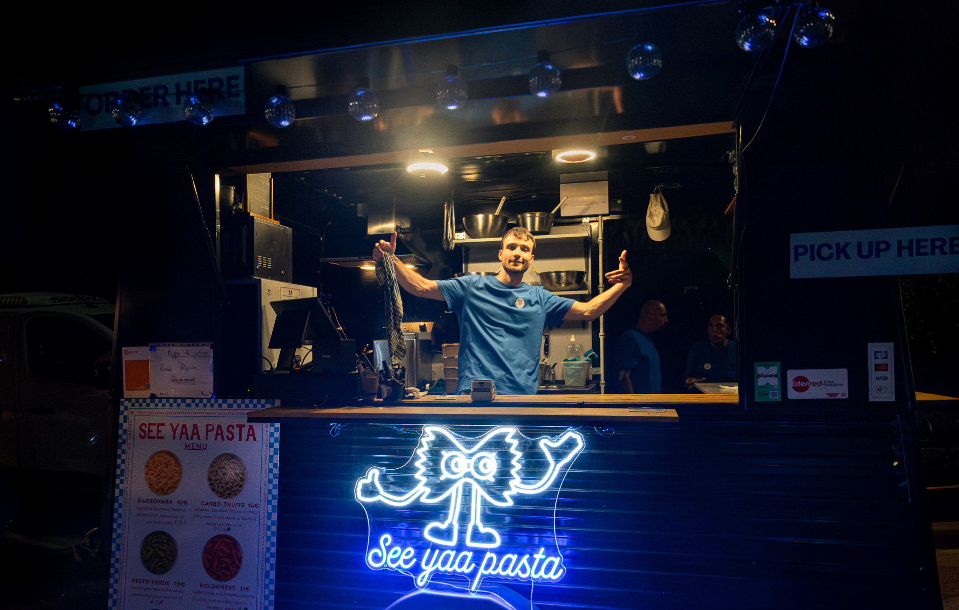 Damien salue depuis le food truck See Yaa Pasta, enseigne néon